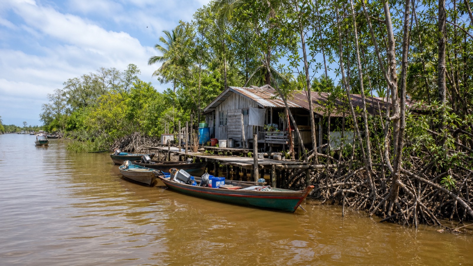 Small boats moored at a wooden jetty in front of riverside stilt houses